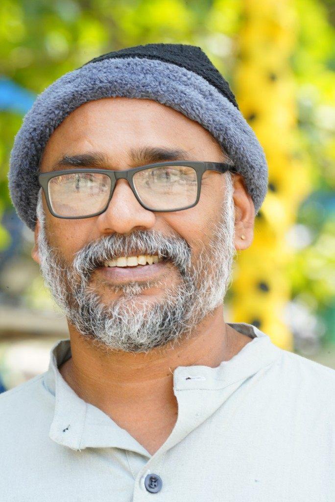 Close portrait of O.P. Suresh, wearing glasses and a grey and black cap.