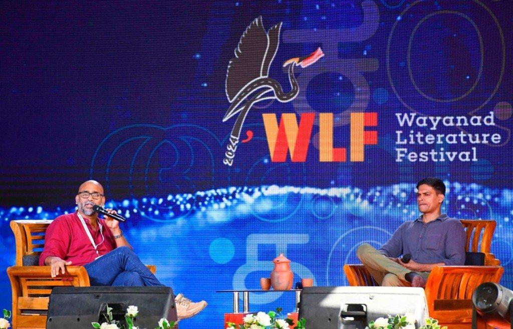 O.P. Suresh speaking on stage at the Wayanad Literature Festival. The screen reads WLF 2024.